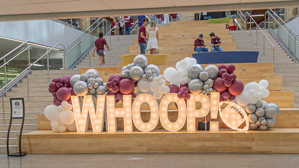 Balloons and large light-up letters saying WHOOP sit on wooden stairs.
