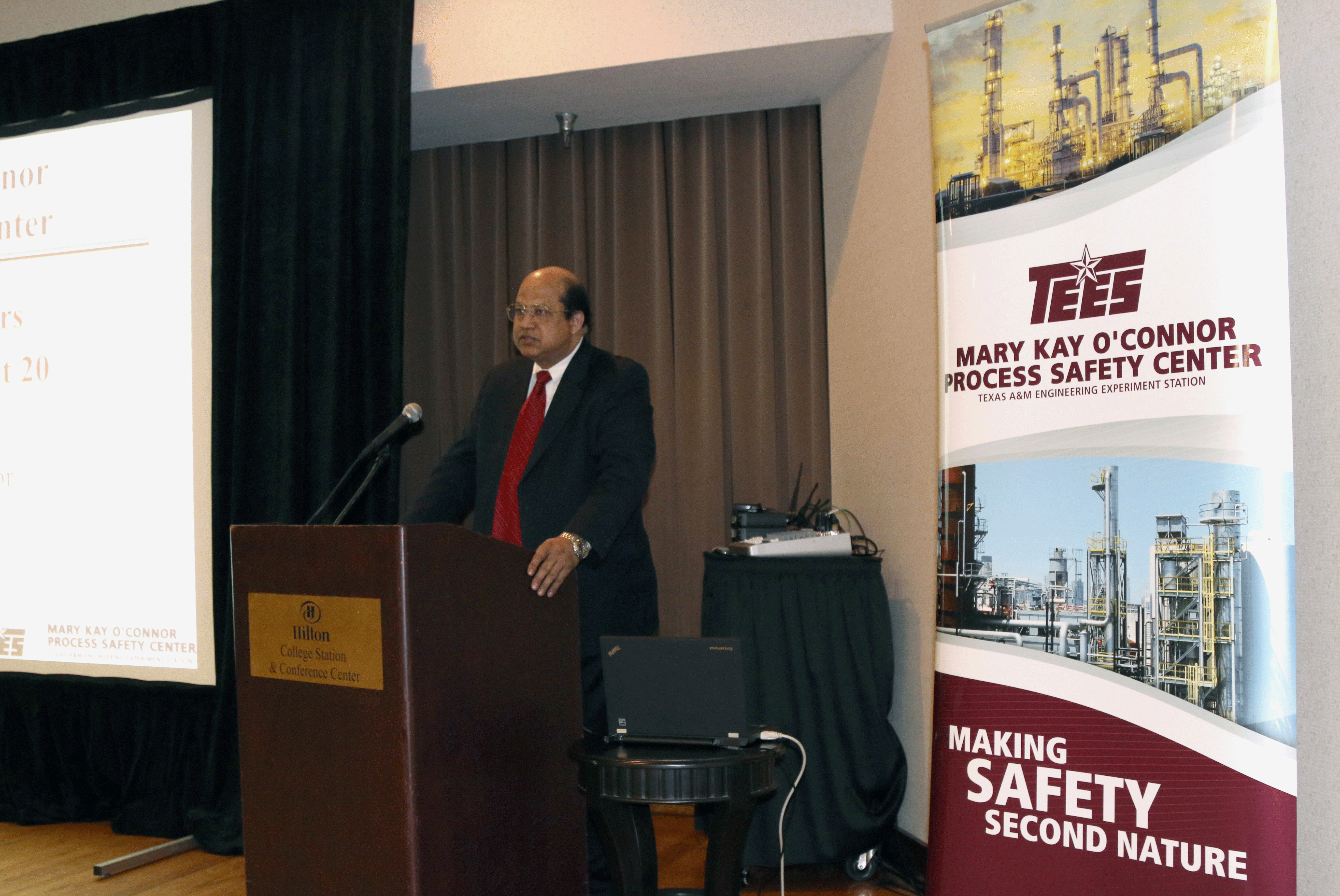 Dr. Sam Mannan speaking on the podium with TEES Mary Kay O'Conner Process Safety Center banner displayed on the side.