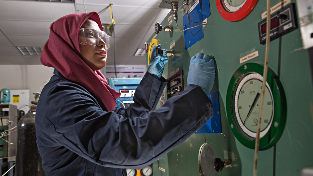Woman wearing a hijab and goggles, working in a lab.