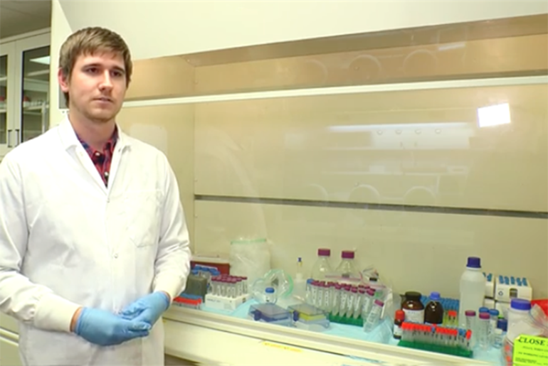Researcher in lab, standing next to multiple sets of test tubes