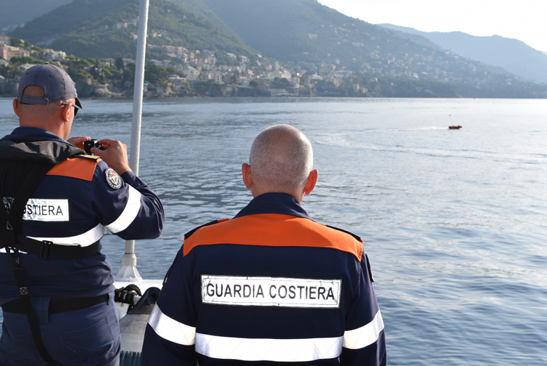Italian Coast Guards Wearing Jackets Entitled Guardia Costiera And Overlooking A Mass Body Of Water
