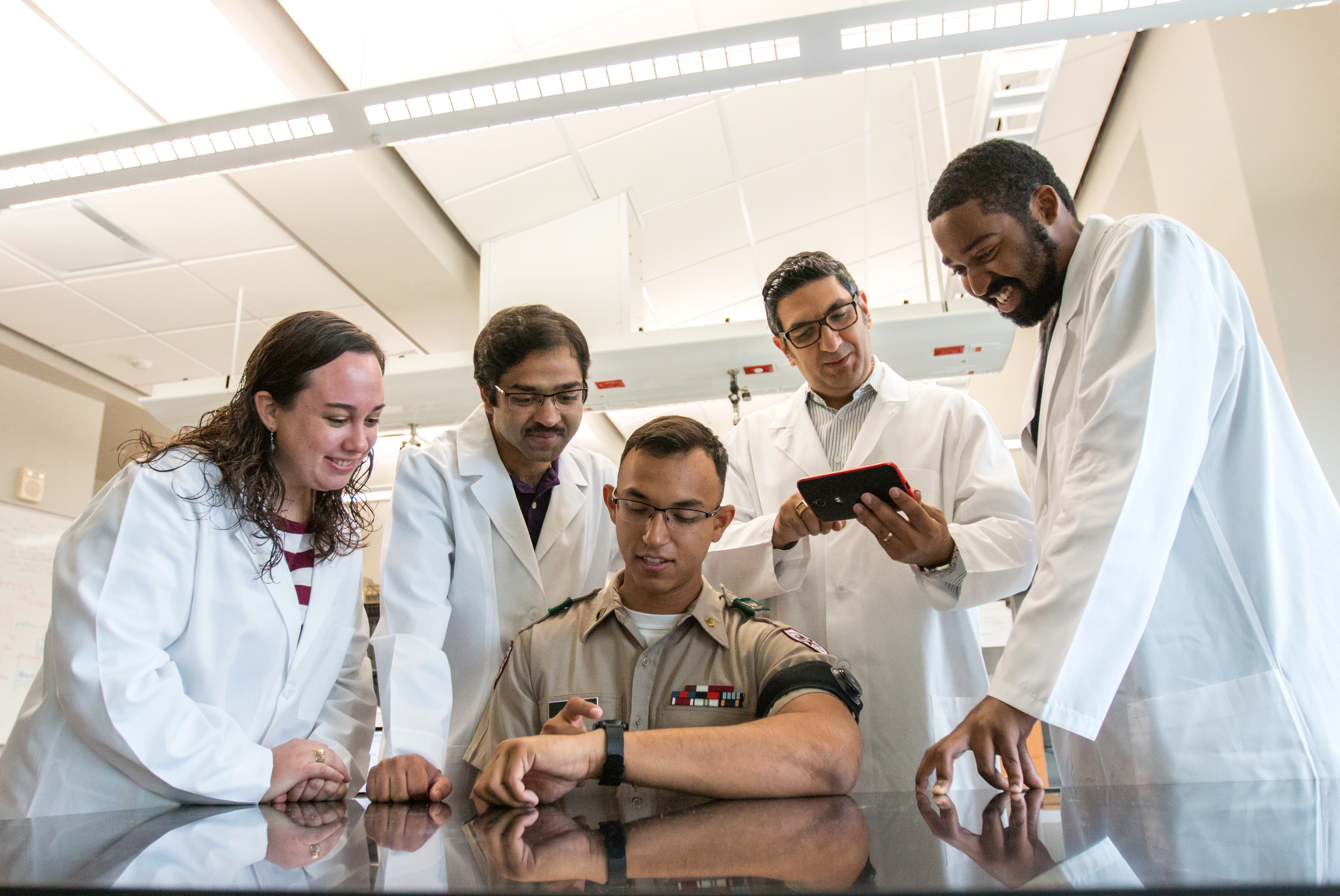 Dr. Sasangohar looking at a smart phone with other researchers and man in uniform is looking at a smart watch.