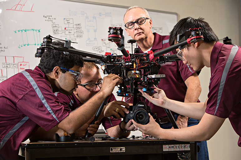 Dr. John Valase and three students working on a drone looking equipment with camera.