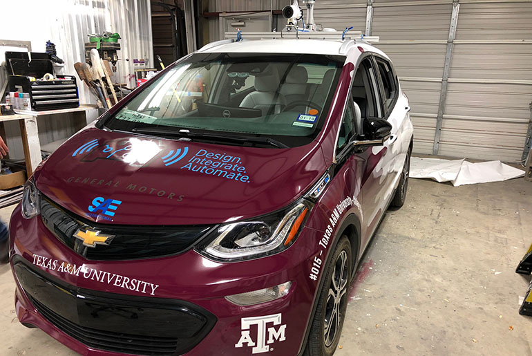 Maroon colored autonomous vehicle with A&amp;M logos.