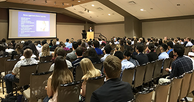 Wide shot of a large group of students listening to a presentation.