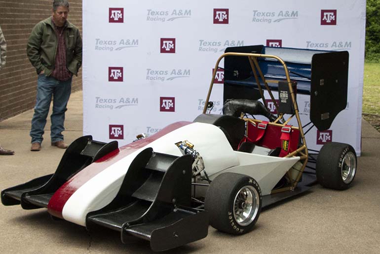 Texas A&amp;M’s Formula SAE car on a display, and a man looking at the vehicle.