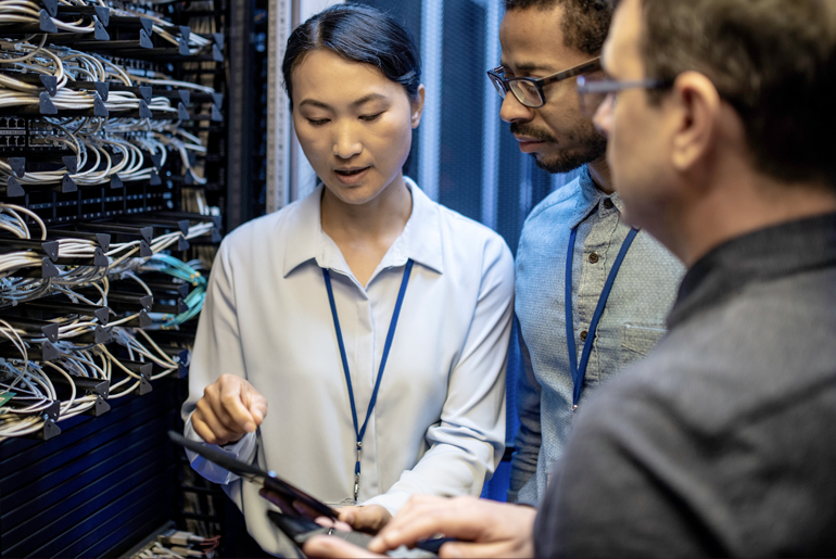 A woman and two men discussing in front of network server.