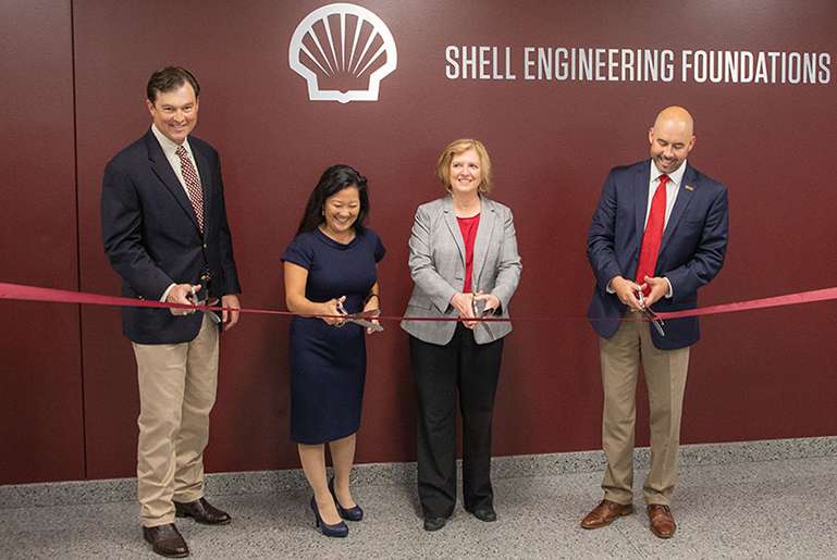 Four individuals are about to cut a red ribbon in front of a wall with words Shell Engineering Foundations