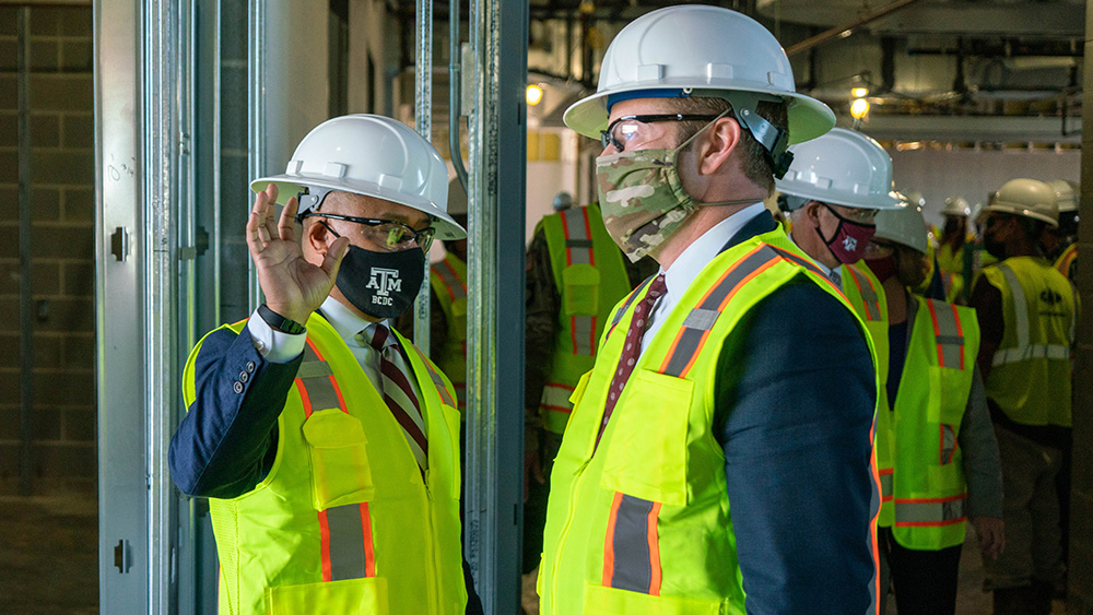 Ross Guieb talking to Ryan D. McCarthy during a tour at the Research Integration Center, with both wearing hard hats, construction vests and masks.