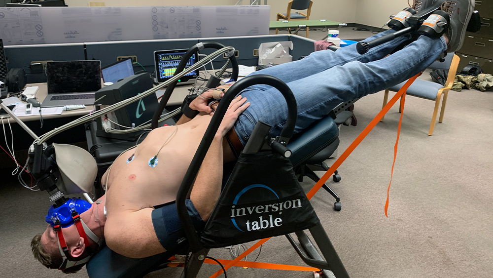 Shirtless man wearing jeans strapped into an inversion table.