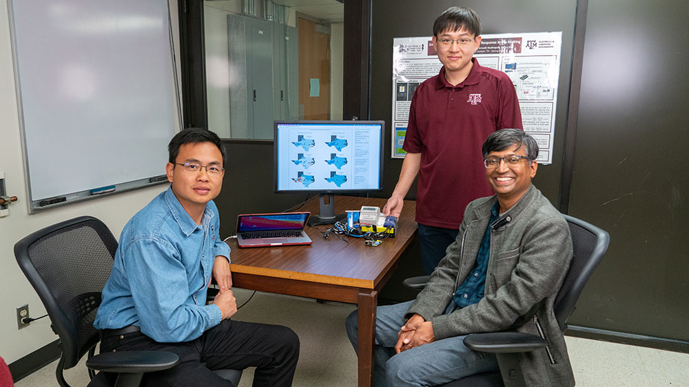 Dr. Le Xie, Dr. Srinivas Shakkottai and Dr. Ki-Yeob Lee sitting around desk with computer showing map of Texas electric grid