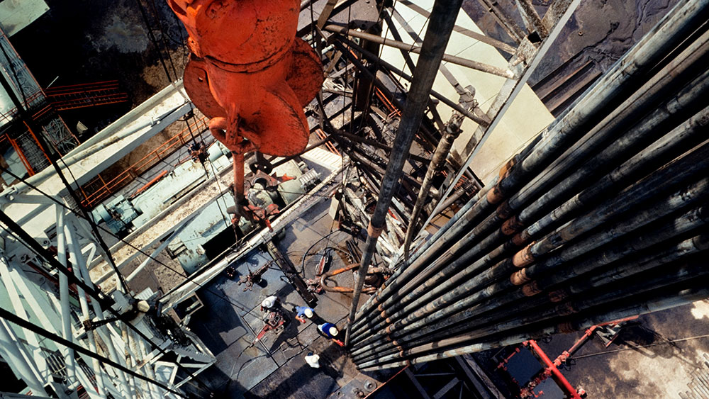 Four workers wearing hard hats on a drilling platform as seen from high above in the rig scaffolding.