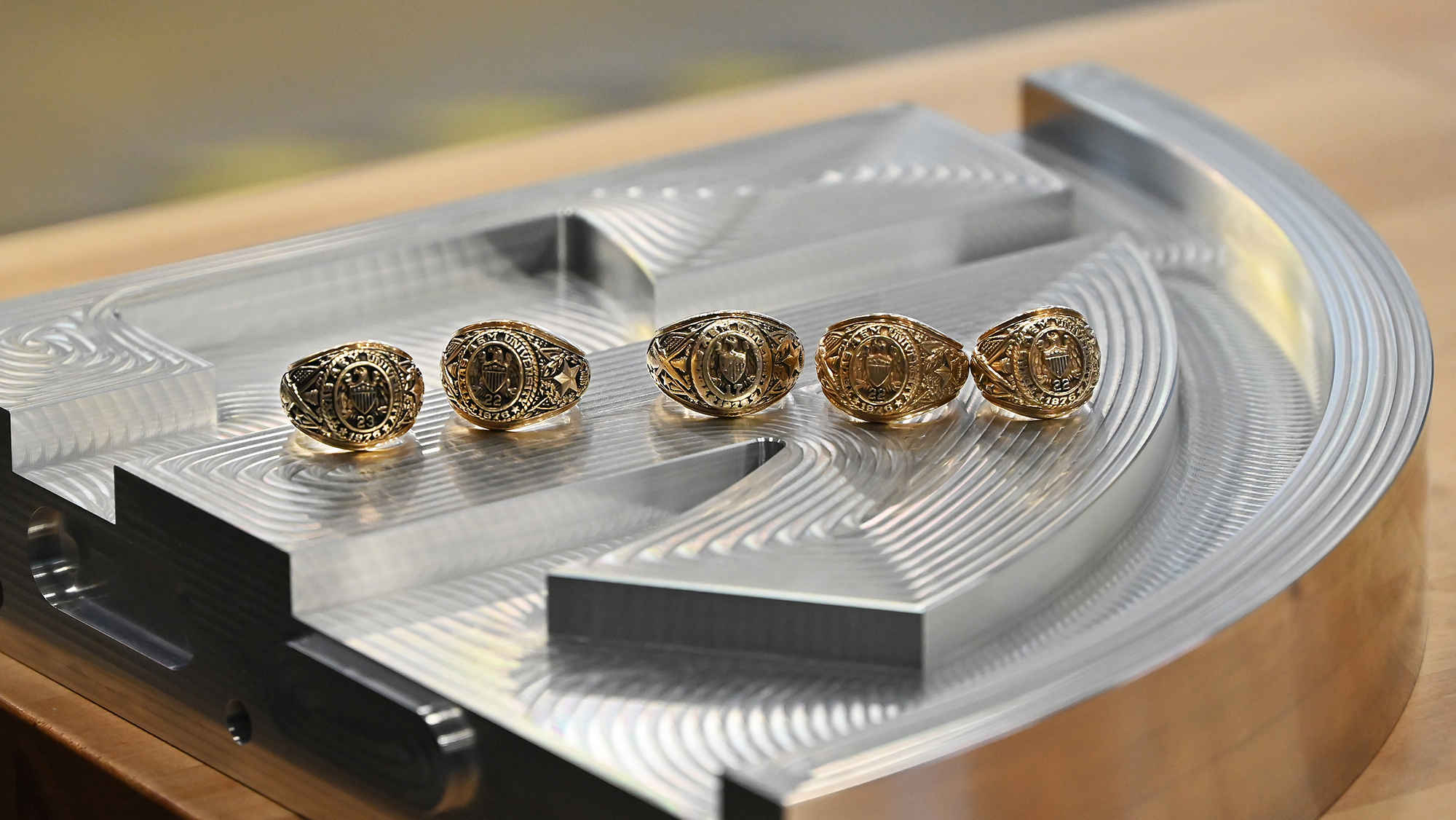 Five Aggie rings sit atop an aluminum plate, the upper right-hand corner of the Southeastern Conference logo.