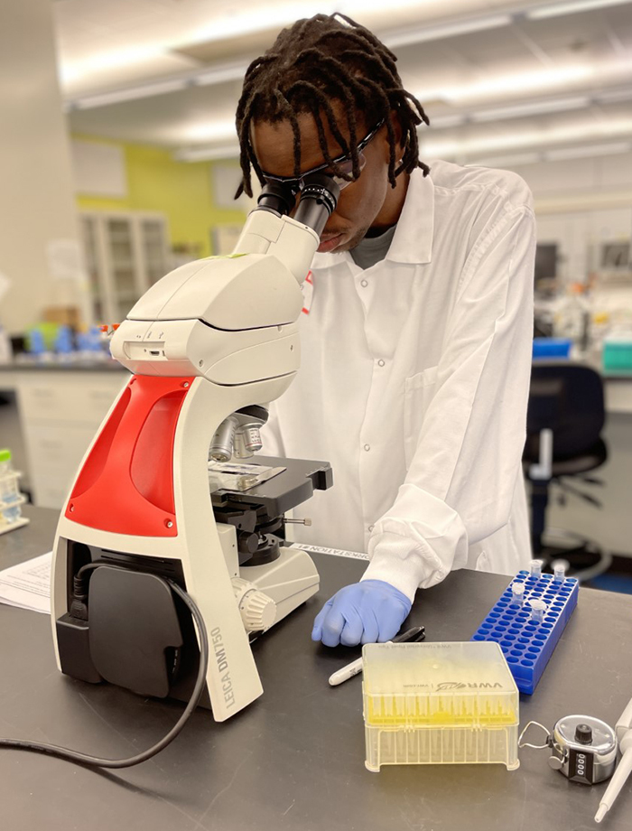 Student in a white lab coat using a microscope.