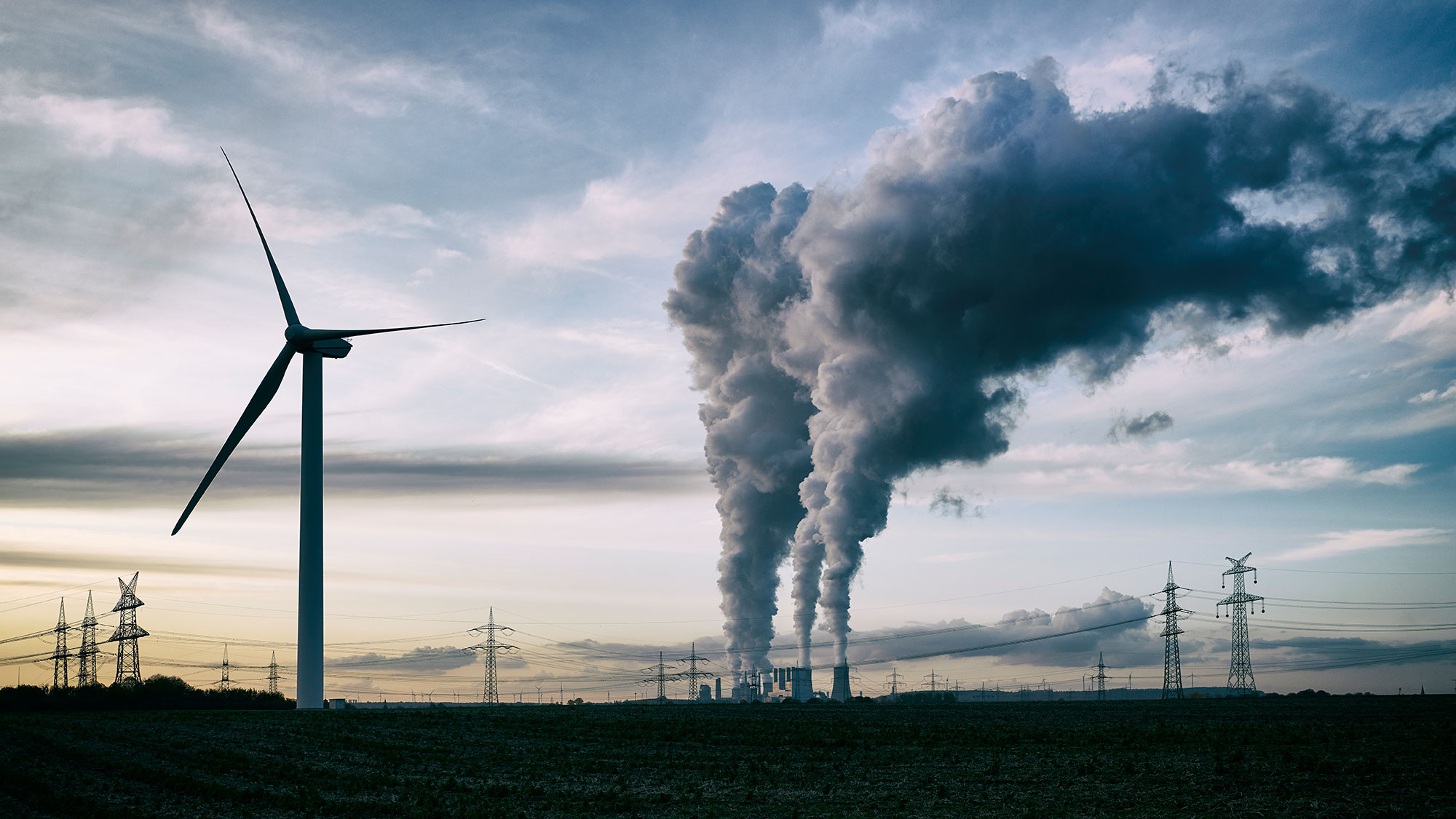 Single wind turbine, a coal-burning power plant with pollution and electricity pylons in the background.
