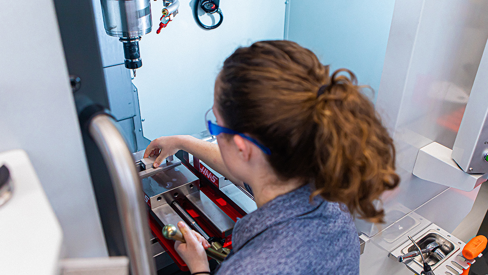 Overhead photo of woman fixing metal object inside a CNC machine. 