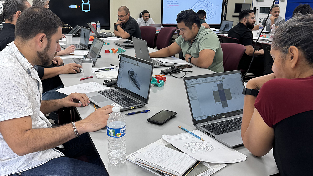 Adults sit around a table working on laptop computers while creating projects in a CAD 3D rendering program. 